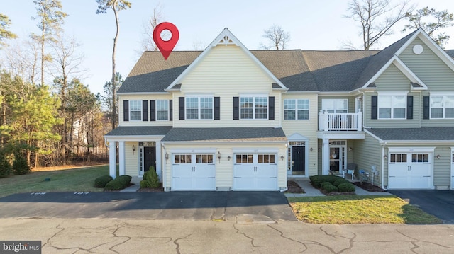 townhome / multi-family property with a shingled roof, an attached garage, a balcony, driveway, and a front lawn