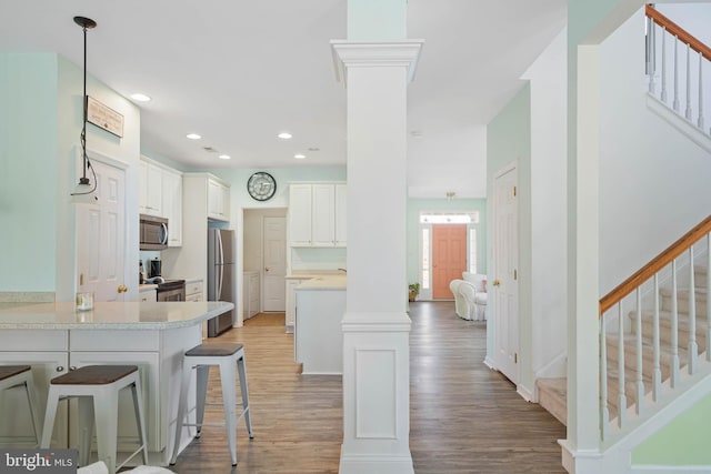 kitchen featuring a breakfast bar area, stainless steel appliances, light countertops, light wood-style floors, and ornate columns