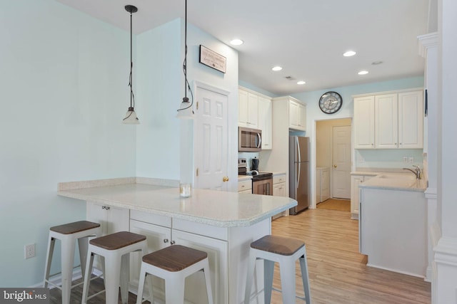 kitchen with light wood finished floors, a breakfast bar area, a peninsula, stainless steel appliances, and a sink