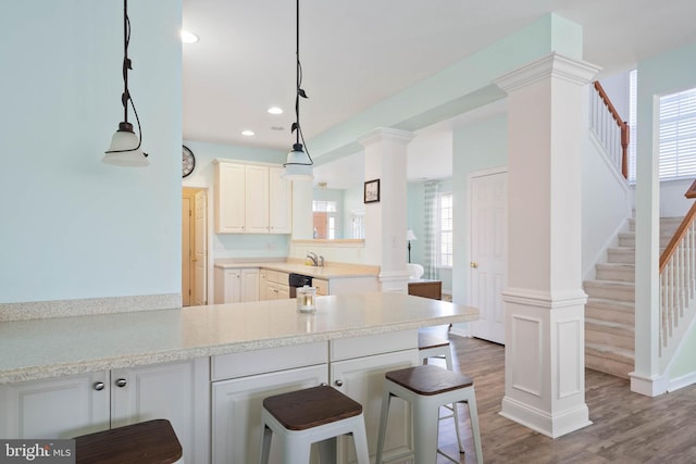 kitchen with a peninsula, ornate columns, light countertops, and wood finished floors