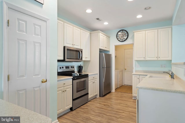 kitchen featuring stainless steel appliances, a sink, light countertops, light wood-type flooring, and washing machine and clothes dryer