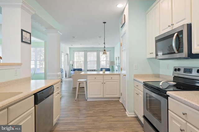 kitchen with open floor plan, stainless steel appliances, light countertops, light wood-type flooring, and ornate columns