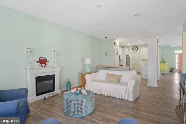 living room featuring recessed lighting, wood finished floors, baseboards, a glass covered fireplace, and decorative columns