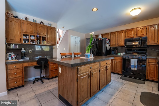 kitchen with light tile patterned floors, built in desk, black appliances, a kitchen island, and decorative backsplash