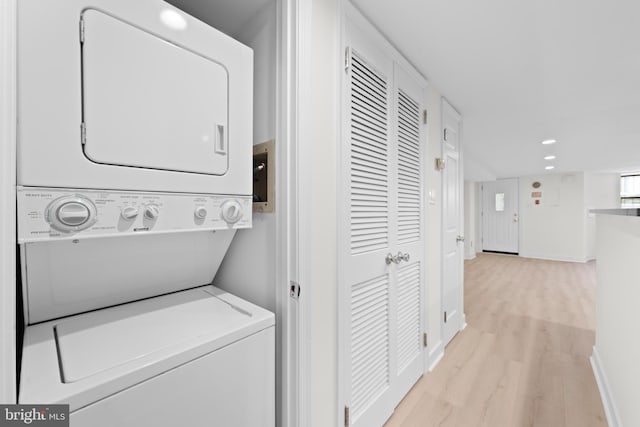 washroom with stacked washer / drying machine and light hardwood / wood-style flooring