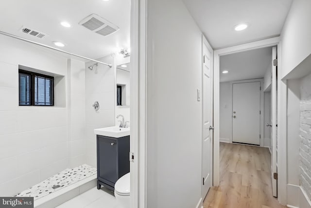 bathroom with tiled shower, vanity, toilet, and wood-type flooring