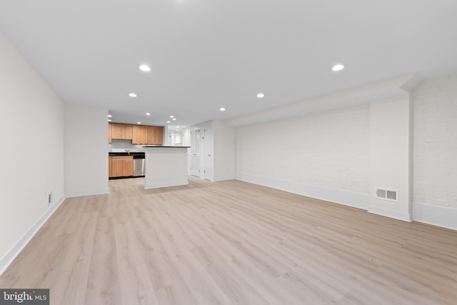 unfurnished living room with brick wall and light hardwood / wood-style floors