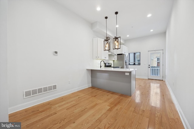 kitchen featuring a breakfast bar, white cabinetry, decorative light fixtures, light hardwood / wood-style floors, and kitchen peninsula