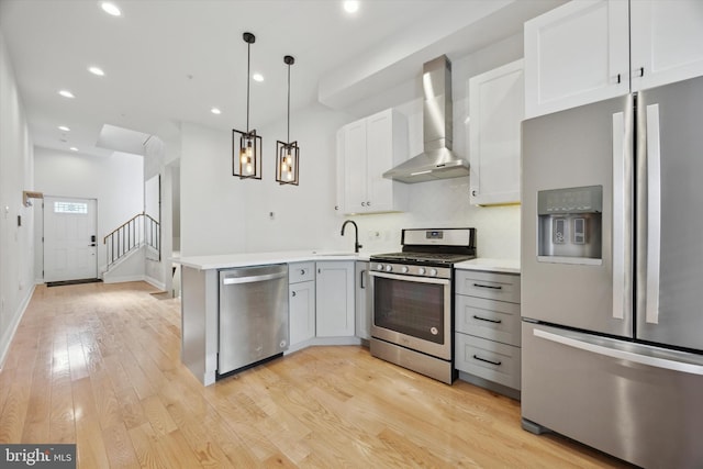 kitchen featuring white cabinetry, kitchen peninsula, hanging light fixtures, appliances with stainless steel finishes, and wall chimney range hood