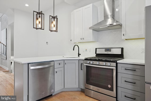 kitchen with appliances with stainless steel finishes, sink, white cabinetry, pendant lighting, and wall chimney exhaust hood