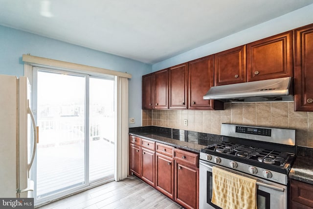 kitchen with tasteful backsplash, dark stone countertops, white refrigerator, stainless steel gas range oven, and light hardwood / wood-style flooring