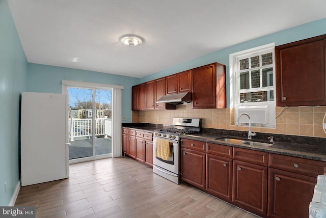 kitchen featuring sink, dark stone countertops, tasteful backsplash, gas stove, and white fridge