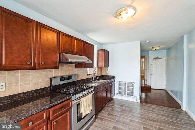 kitchen featuring stainless steel gas stove, sink, dark stone countertops, decorative backsplash, and light hardwood / wood-style flooring