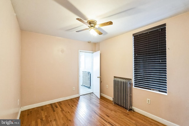 empty room with hardwood / wood-style floors, radiator heating unit, and ceiling fan