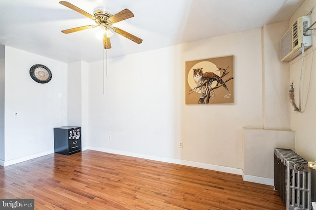 spare room with hardwood / wood-style flooring, radiator, a wall mounted AC, and ceiling fan