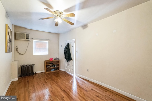 unfurnished bedroom featuring hardwood / wood-style flooring, ceiling fan, radiator, and a wall unit AC