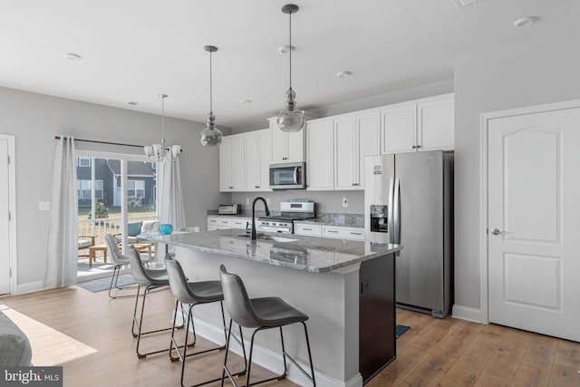 kitchen with white cabinetry, decorative light fixtures, stainless steel appliances, light stone countertops, and a kitchen island with sink