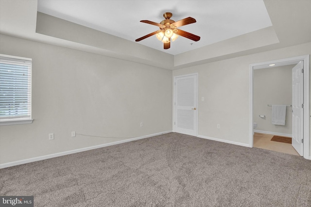 unfurnished room featuring ceiling fan, a tray ceiling, and light carpet