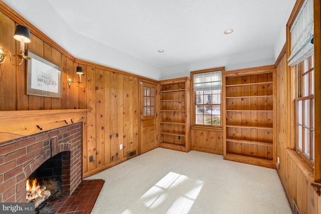 unfurnished living room with a brick fireplace, carpet, and wooden walls