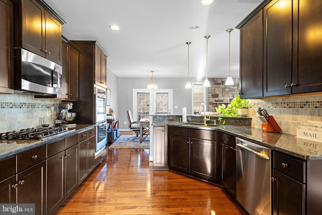 kitchen with decorative light fixtures, sink, dark stone countertops, dark brown cabinetry, and stainless steel appliances