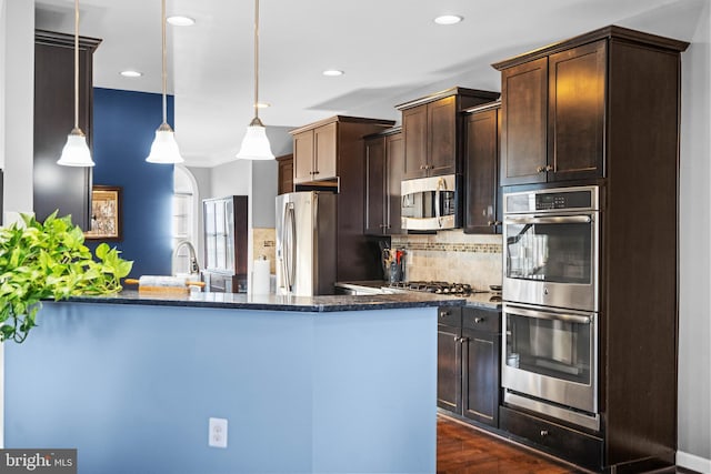 kitchen with tasteful backsplash, decorative light fixtures, dark brown cabinets, appliances with stainless steel finishes, and kitchen peninsula