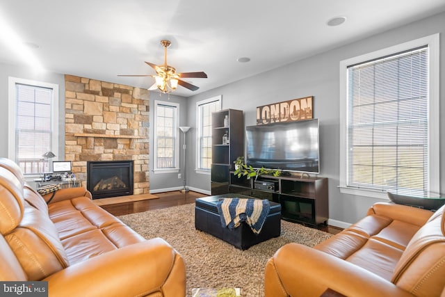 living room featuring a stone fireplace, hardwood / wood-style floors, and ceiling fan