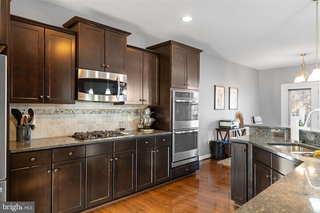 kitchen with sink, wood-type flooring, dark stone countertops, appliances with stainless steel finishes, and decorative backsplash