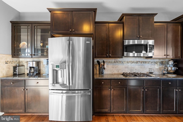 kitchen with hardwood / wood-style flooring, stainless steel appliances, decorative backsplash, and dark stone countertops