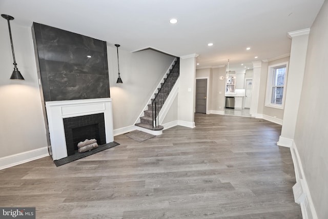 unfurnished living room featuring wood finished floors, stairway, a tile fireplace, and crown molding