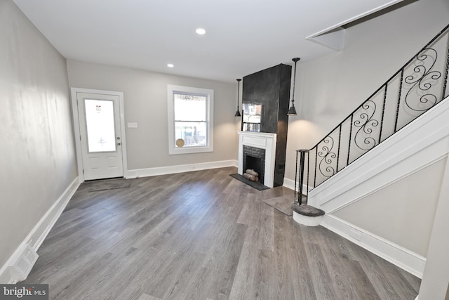 unfurnished living room with baseboards, wood finished floors, stairs, a fireplace, and recessed lighting