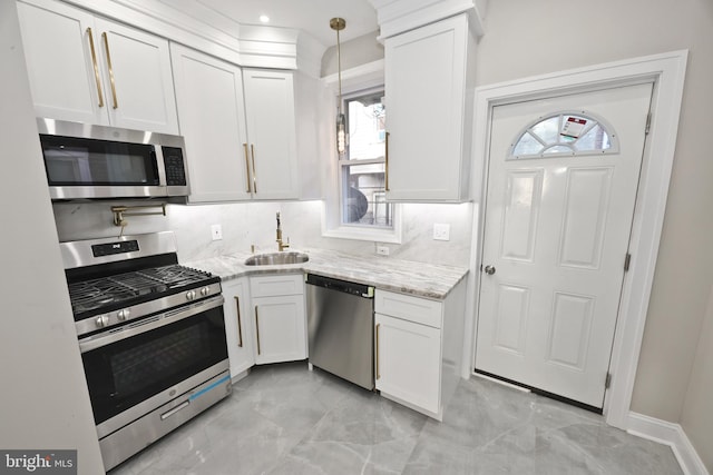 kitchen with light stone counters, decorative light fixtures, stainless steel appliances, white cabinets, and a sink