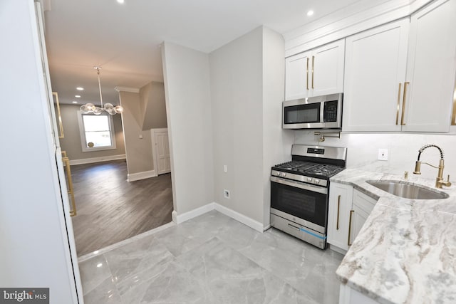 kitchen with light stone counters, stainless steel appliances, a sink, white cabinets, and an inviting chandelier