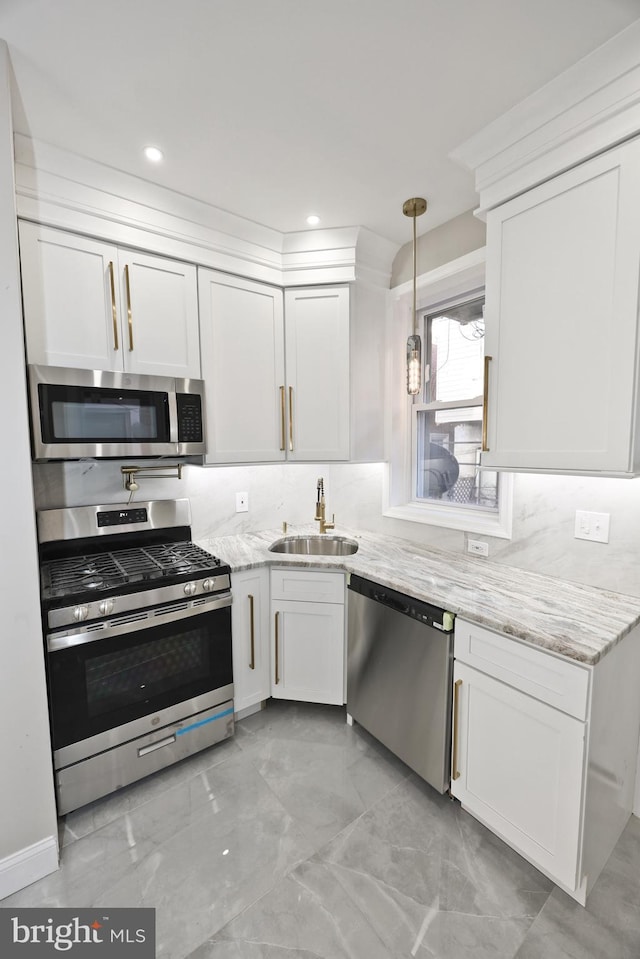 kitchen featuring white cabinets, decorative backsplash, light stone counters, stainless steel appliances, and a sink