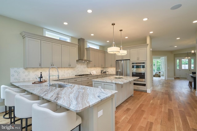 kitchen with pendant lighting, sink, appliances with stainless steel finishes, kitchen peninsula, and wall chimney exhaust hood