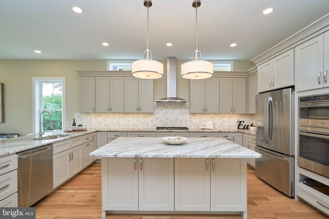 kitchen featuring light stone counters, wall chimney range hood, stainless steel appliances, and a center island