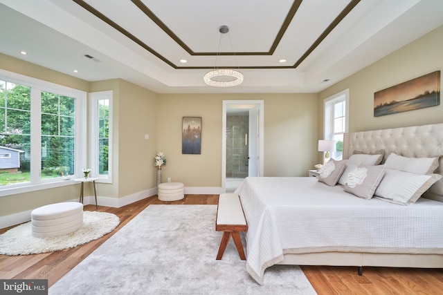 bedroom with connected bathroom, light hardwood / wood-style floors, and a raised ceiling