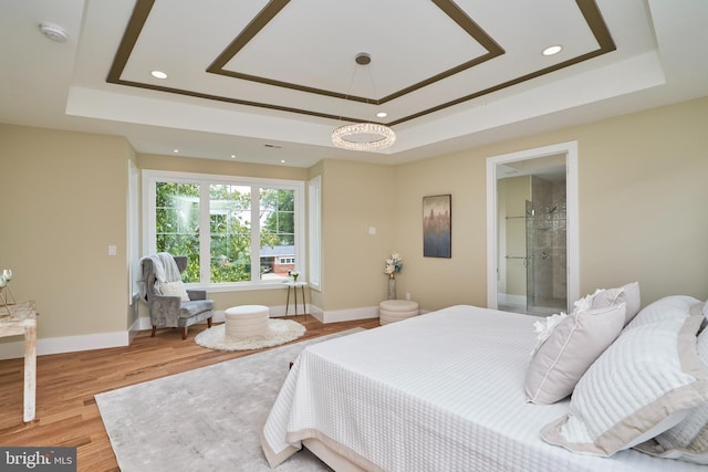 bedroom featuring ensuite bath, light wood-type flooring, and a tray ceiling