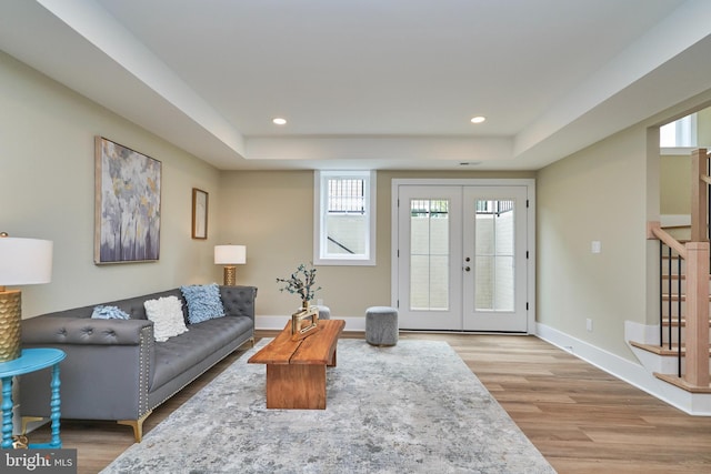 living room featuring a raised ceiling, light wood-type flooring, and french doors