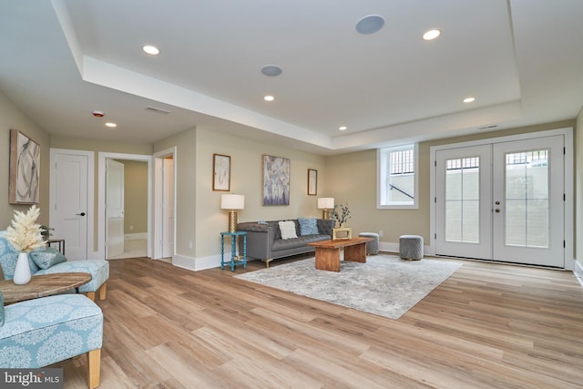 living room featuring a tray ceiling, light hardwood / wood-style flooring, and french doors