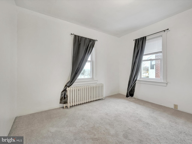 empty room featuring radiator, light colored carpet, and a healthy amount of sunlight