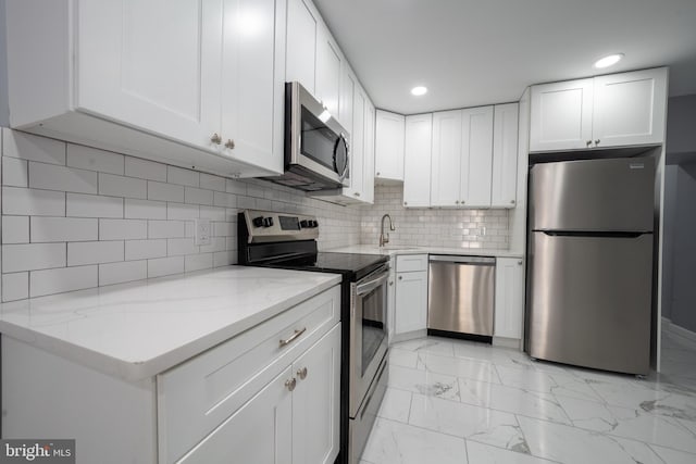 kitchen featuring sink, white cabinets, decorative backsplash, light stone counters, and stainless steel appliances