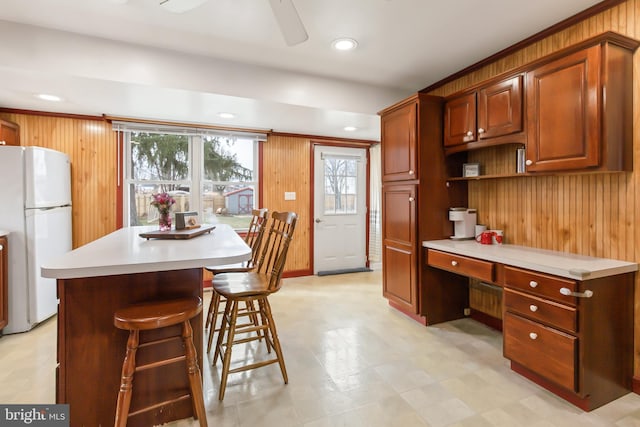 kitchen with a breakfast bar, wood walls, built in desk, white refrigerator, and a kitchen island