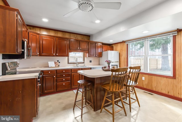 kitchen with a kitchen bar, sink, a center island, white refrigerator, and wooden walls