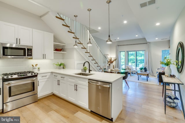 kitchen with sink, white cabinetry, stainless steel appliances, light hardwood / wood-style floors, and decorative light fixtures