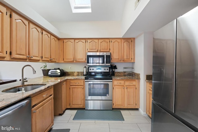 kitchen with sink, light stone counters, a skylight, light tile patterned floors, and appliances with stainless steel finishes