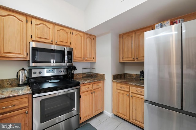 kitchen with appliances with stainless steel finishes, light tile patterned floors, and dark stone counters