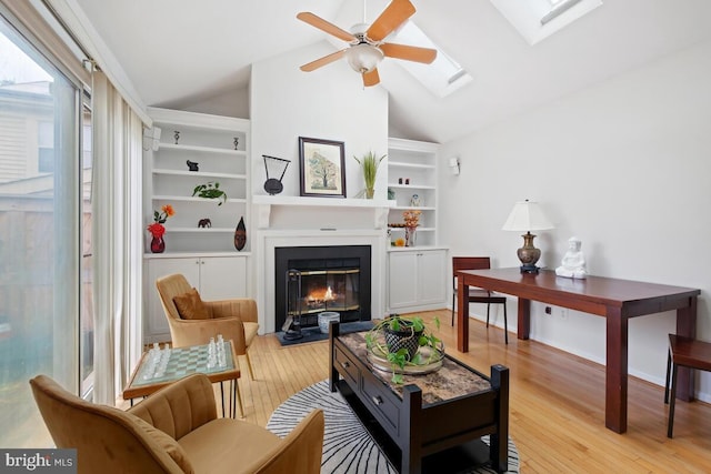 sitting room featuring built in features, lofted ceiling with skylight, and light hardwood / wood-style flooring