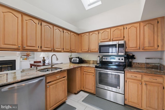 kitchen featuring sink, light tile patterned floors, stone counters, a skylight, and stainless steel appliances