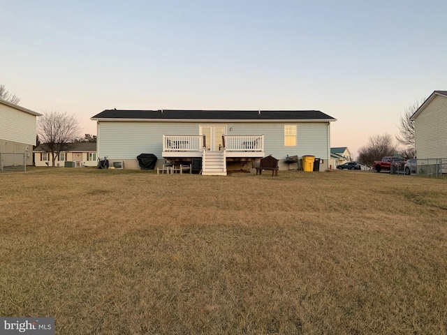 back house at dusk featuring a deck and a lawn