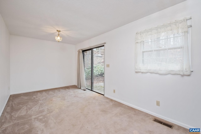 spare room featuring light carpet, a textured ceiling, and an inviting chandelier